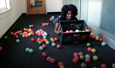 a woman lying on the floor, dumping plastic balls out of a box onto the floor